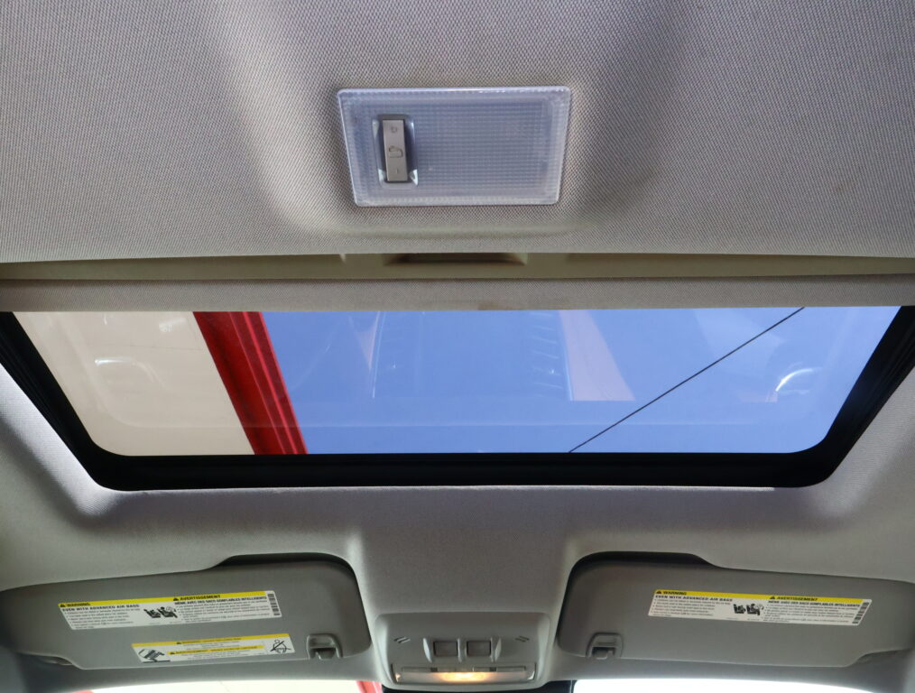 Interior of a car ceiling with a rectangular overhead light panel centered on the headliner and a sunroof letting in blue sky outside.