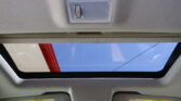 Interior of a car ceiling with a rectangular overhead light panel centered on the headliner and a sunroof letting in blue sky outside.