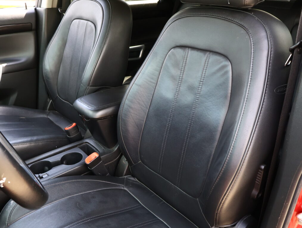 Front interior of a car showing black leather seats and center console with cup holders.