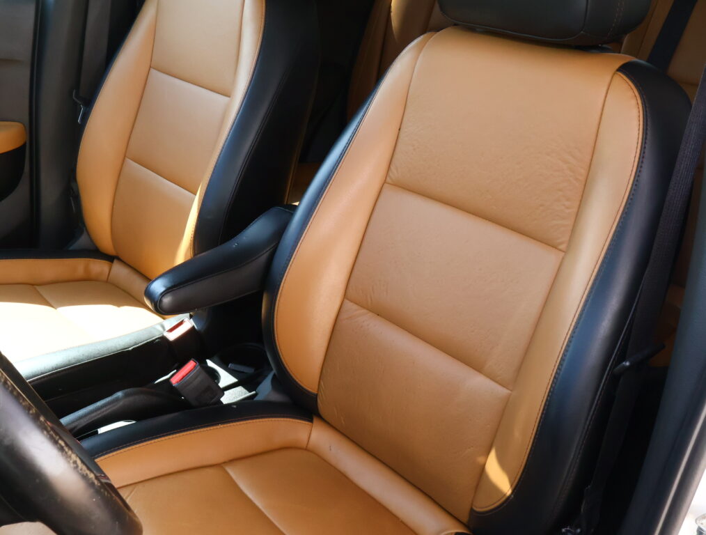 Tan leather car seats with black trim and visible stitching inside a vehicle cabin, showing a front passenger area