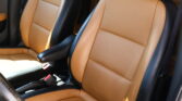 Tan leather car seats with black trim and visible stitching inside a vehicle cabin, showing a front passenger area