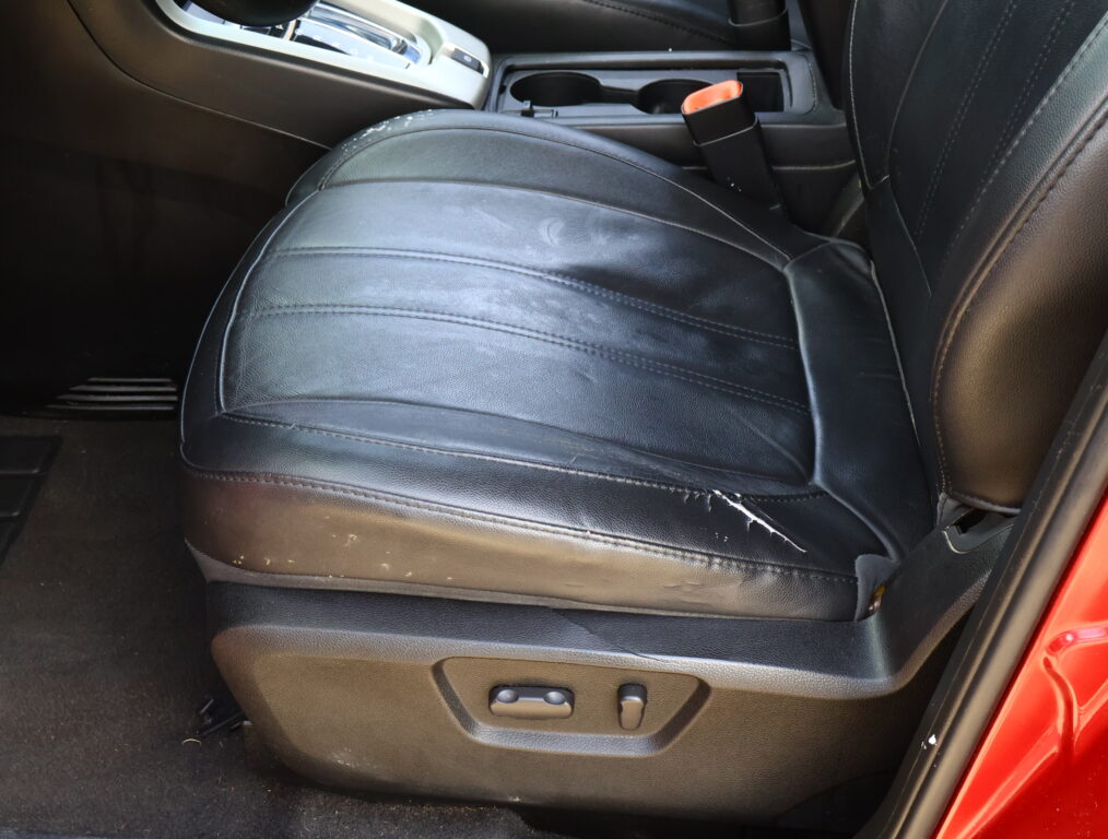 Black leather car seat with light scuffs, center console cup holders, and a hint of red door frame edge.