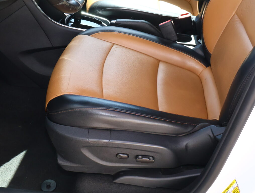 Rear car seat row in dark leather with stitched seams and patterned fabric inserts, showing three seating positions and seat belts.