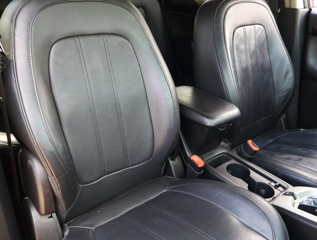 Black leather car seats with a center console and orange seat belt buckles visible between the front seats.