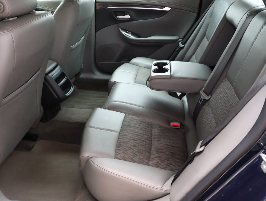 Rear passenger seating area of a car with gray leather upholstery and a center armrest that folds down, containing two cup holders.