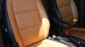 Tan leather car seats with black side panels and visible seat belts inside a vehicle.