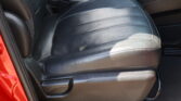 Close-up of a black leather car seat with the center console and orange-seat-belt buckle nearby, red door frame visible at left.