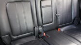 Leather car back seat with two visible seat belts and red buckles in a dark interior.