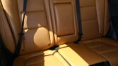 Tan leather car backseat with three seat belts and headrests visible in a sunlit interior.