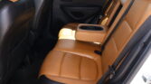 Interior of a car rear seat area with tan leather seats, black door panel, and a center armrest featuring cup holders