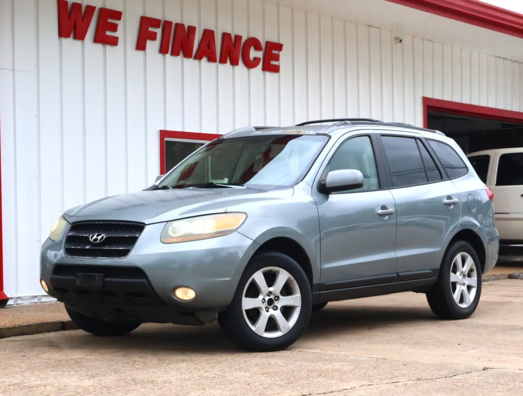 Silver Hyundai SUV parked in front of a white building with red trim at a car dealership, 'WE FINANCE' sign visible.