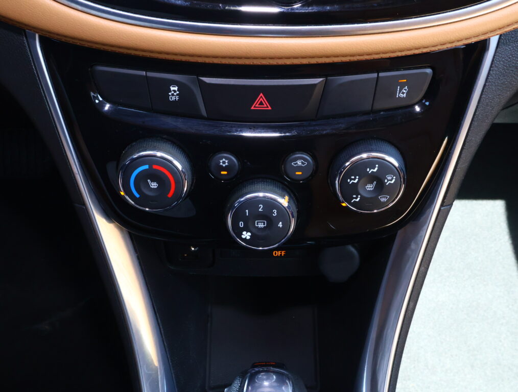 Car center console with hazard button highlighted in red, traction-control-off button, and three climate-control dials beneath brown leather trim.