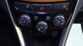 Car center console with hazard button highlighted in red, traction-control-off button, and three climate-control dials beneath brown leather trim.