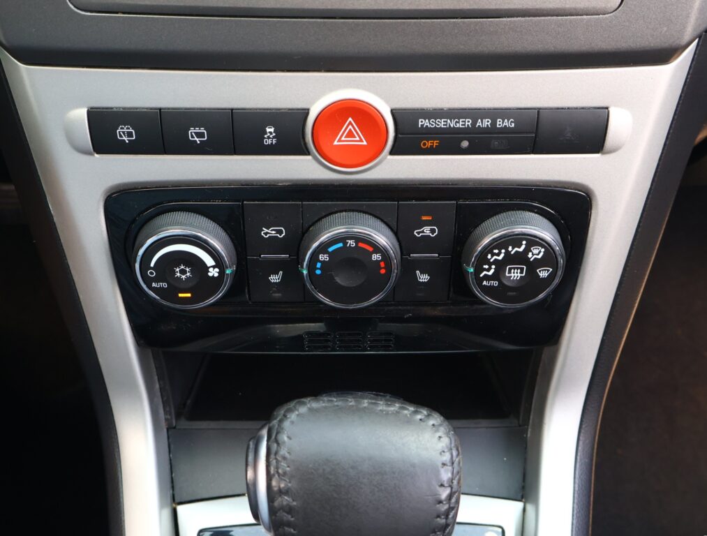 Center console of a car: hazard button flanked by climate control buttons and a leather gear shift boot below.