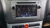 Car infotainment touchscreen showing Now Playing, FM, Phone, and other apps on a dashboard UI