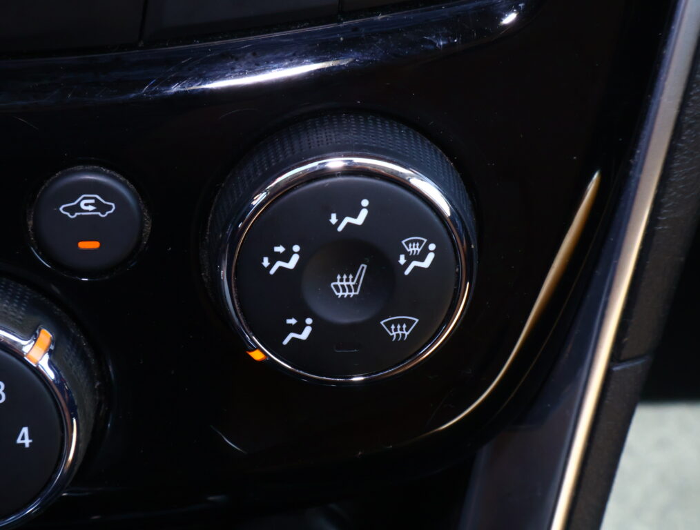 Close-up of a car seat heater dial and nearby controls on a glossy black center console.