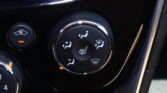 Close-up of a car seat heater dial and nearby controls on a glossy black center console.