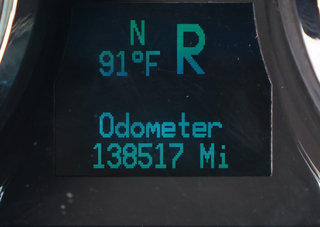 Close-up of a digital car odometer display showing mileage in miles on a dark dashboard.