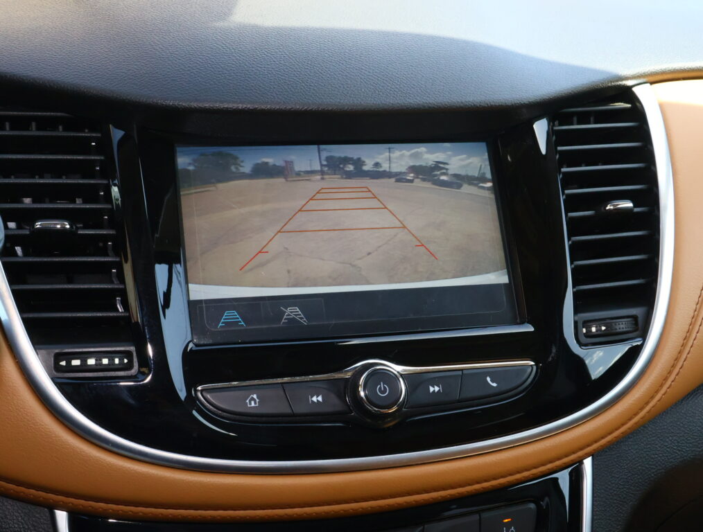 In-car touchscreen showing the rearview camera feed with orange parking guideline lines, surrounded by brown leather dashboard and air vents in a vehicle interior.
