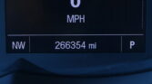 Car dashboard readout showing current speed 0 MPH with NW as direction and an odometer reading of 266,354 miles