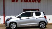 Silver hatchback parked in front of a white wall with a red 'WE FINANCE' sign above the car's roof line.
