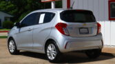 Rear three-quarter view of a silver Chevrolet SUV parked in a dealership lot, with a large sign offering a 12-month/12K-mile warranty above the building.