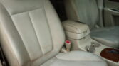 Beige car interior with worn leather seats and a cracked center armrest, showing passenger-side door panel and wood trim.