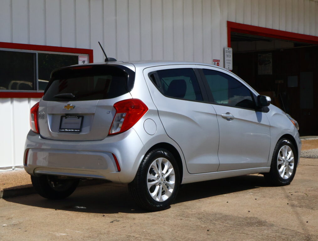 Rear three-quarter view of a silver Chevrolet SUV parked outside a white building with red trim.