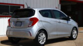 Rear three-quarter view of a silver Chevrolet SUV parked outside a white building with red trim.