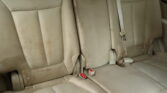 Rear car back seats in tan leather with three seating positions and buckled seat belts visible in the center and sides.