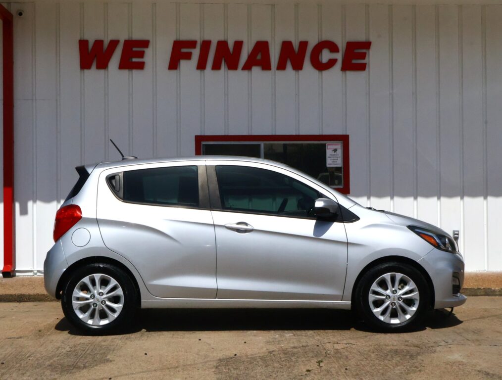Silver hatchback parked in front of a white wall with a red 'WE FINANCE' sign above it.