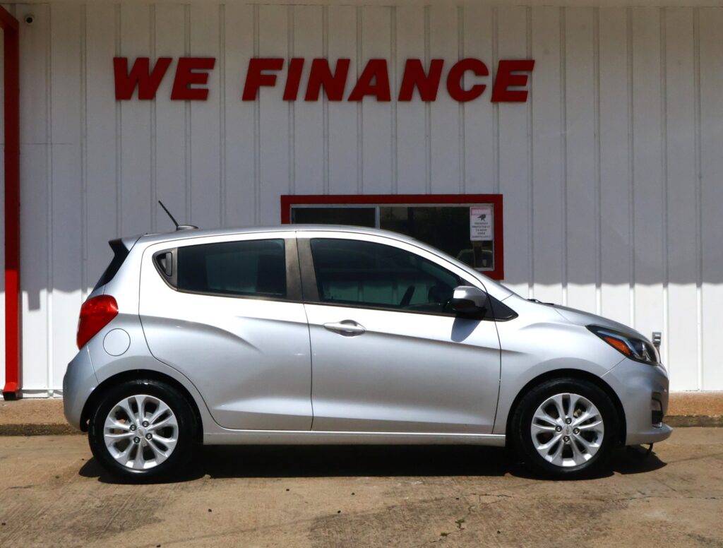Silver hatchback parked in front of a white wall with a red 'WE FINANCE' sign above it.
