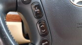 Close-up of steering wheel controls: MODE button, plus/minus volume switch, and MUTE on a black panel with a textured surface, left side of the wheel.
