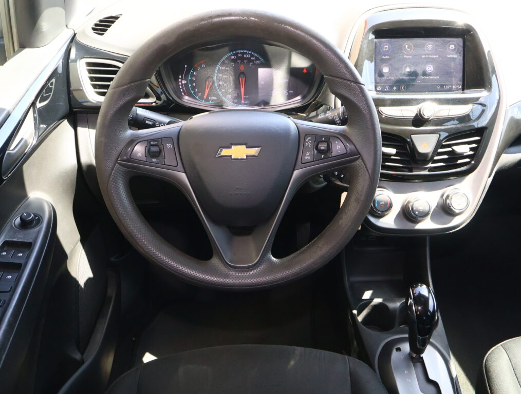 Interior view from the driver seat showing a Chevrolet steering wheel, instrument cluster, and right-side touchscreen display.