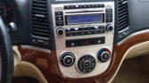 Center dashboard of a Hyundai with a factory radio showing FM radio at 100.3 MHz and round climate control dials below on a beige dashboard with wood trim.