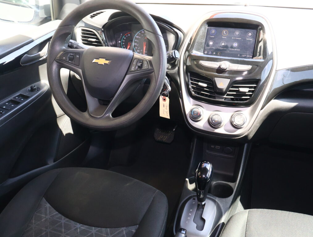 Front interior of a Chevrolet car showing steering wheel, dashboard, and center touchscreen display for infotainment and climate controls, with gear shift nearby.