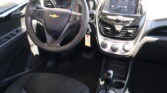 Front interior of a Chevrolet car showing steering wheel, dashboard, and center touchscreen display for infotainment and climate controls, with gear shift nearby.