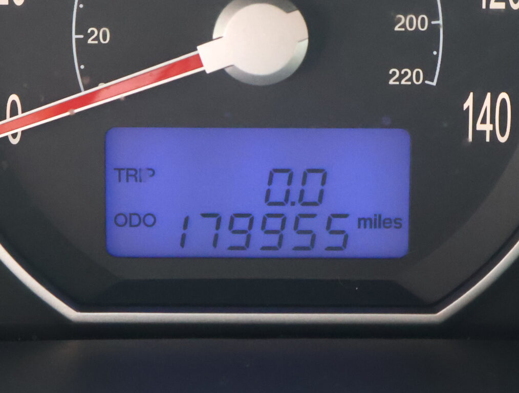 Close-up of a car dashboard: analog speedometer with a red needle around 20 mph, and a blue digital display showing TRIP 0.0 and an odometer reading about 119,955 miles.