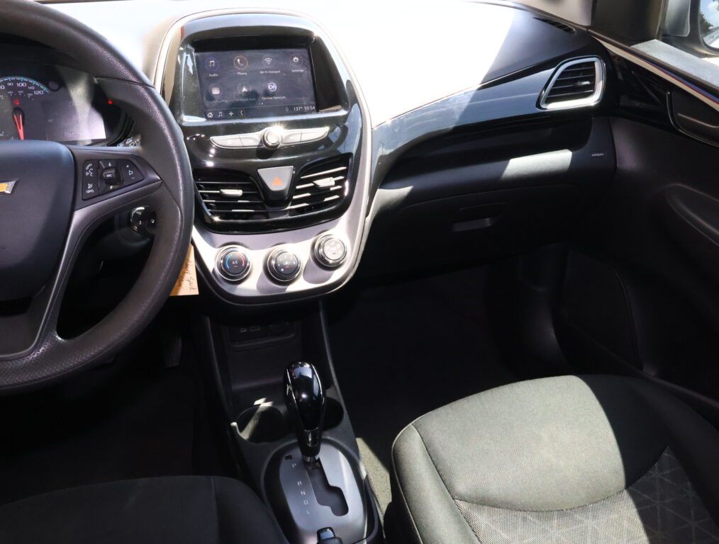 Interior of a car: steering wheel left, central touchscreen display, climate controls, and gear shifter in view.