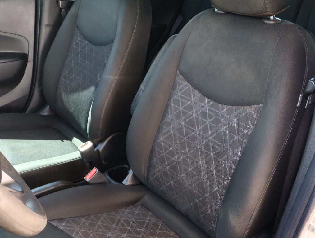 Inside a car showing the dark fabric front seats with geometric stitching and a center console area nearby, in a muted gray interior.