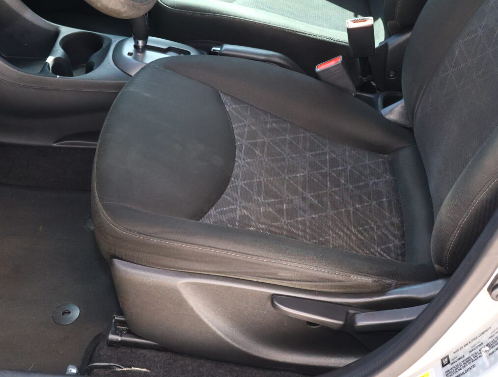 Front seats and center console of a car, with the gear shifter, cup holders, and seat belt buckles visible in a dark interior.