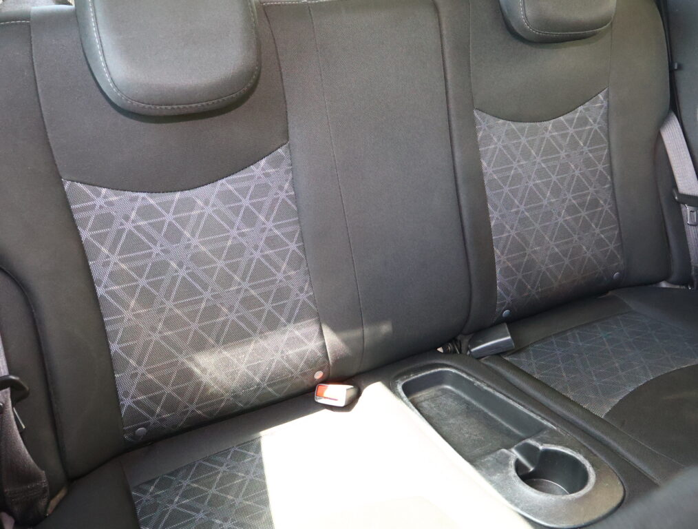 Back seat of a car with black upholstery and patterned fabric panels, headrests visible and a cup holder in the foreground.