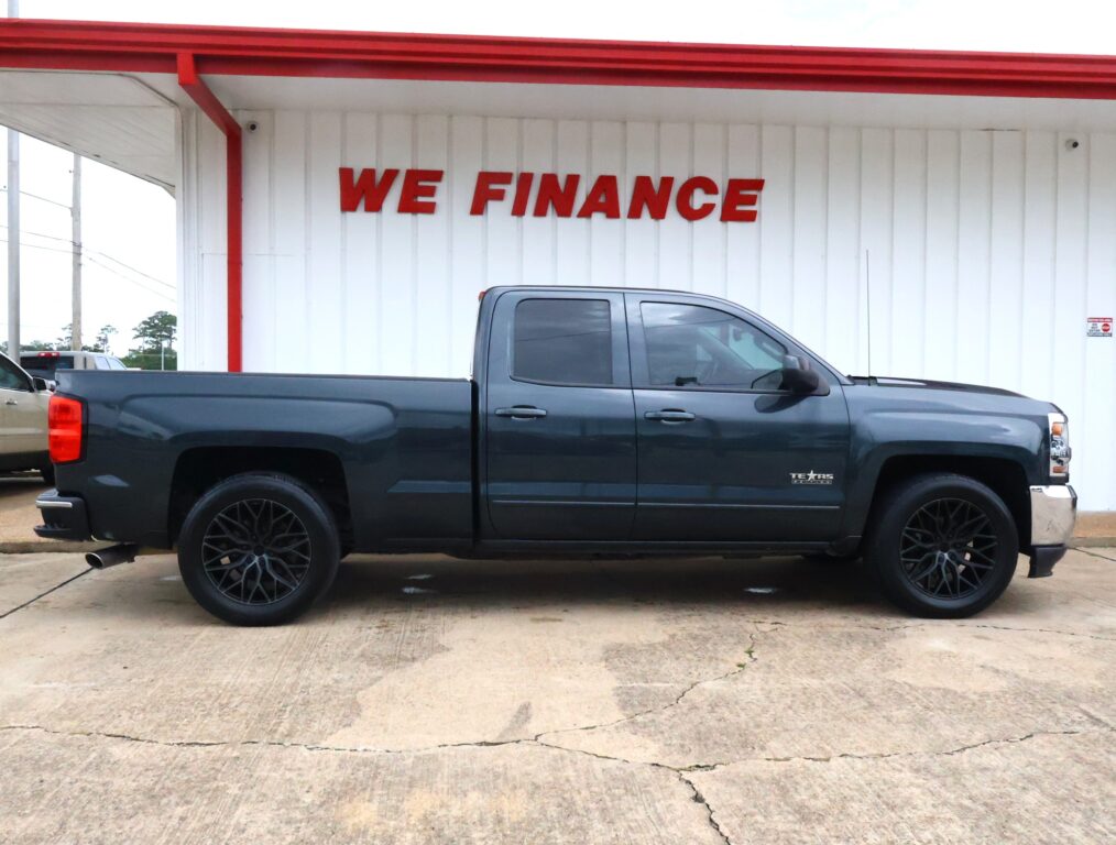 Dark gray pickup truck parked in front of a white wall with a bold red 'WE FINANCE' sign above it.