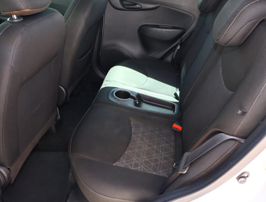 Rear car seat interior with center armrest containing two cup holders, black upholstery, and visible seat belts.