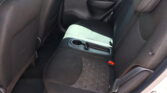 Rear car seat interior with center armrest containing two cup holders, black upholstery, and visible seat belts.