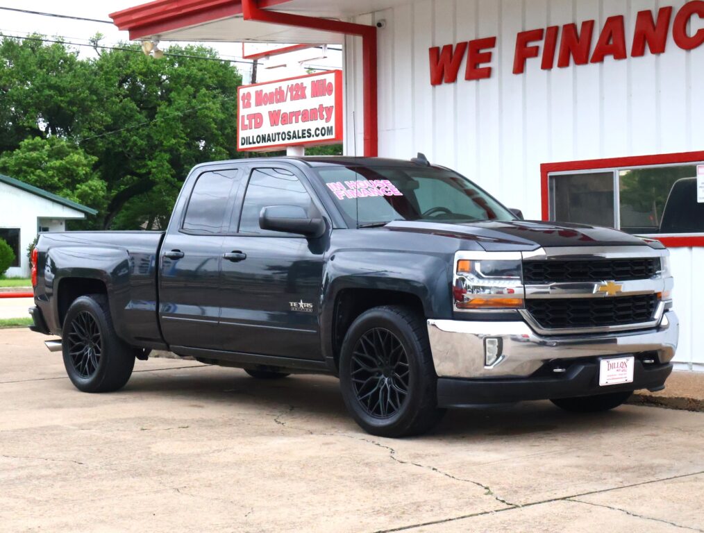 Black Chevrolet Silverado pickup parked in front of a white dealership building with a bold red 'WE FINANCE' sign and a large 'DILLON AUTO SALES' sign nearby. The windshield shows an 'IN HOUSE FINANCE' sticker.