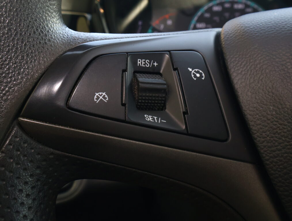 Close-up of a car steering wheel's cruise control panel showing RES/+ and SET/- buttons.