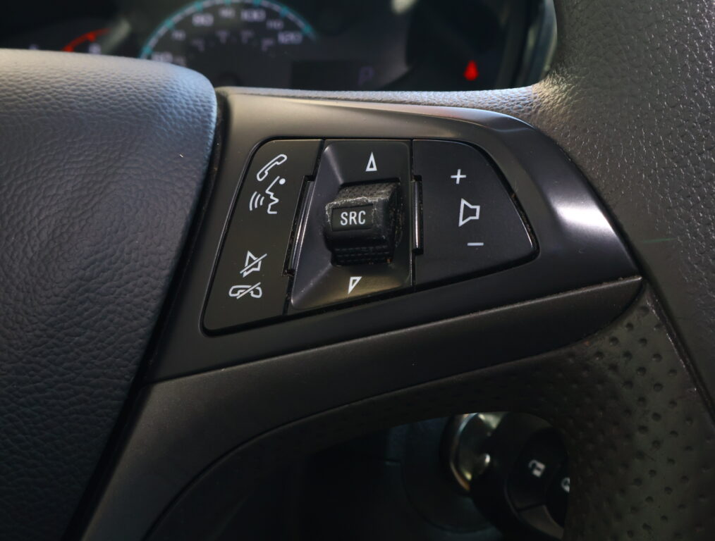 Close-up of steering wheel controls: phone call button, SRC mute area, and volume/arrow buttons on a car’s black dashboard panel.
