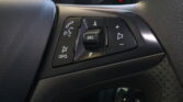 Close-up of steering wheel controls: phone call button, SRC mute area, and volume/arrow buttons on a car’s black dashboard panel.