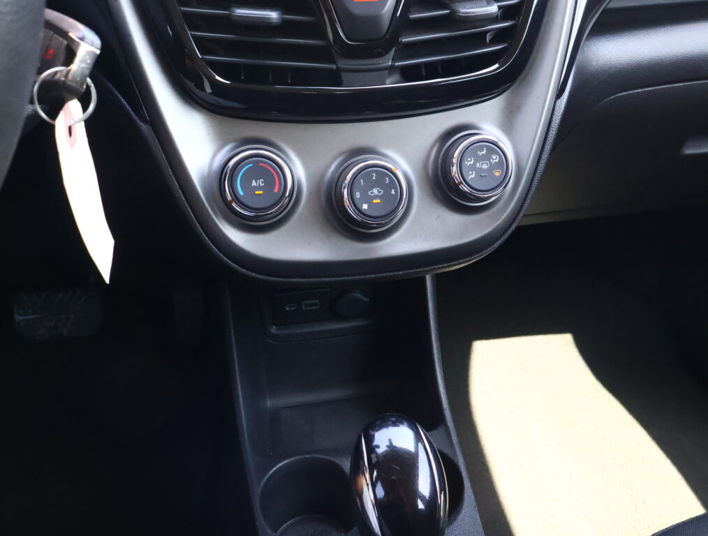 Center console of a car showing three round climate control dials and a glossy gear shifter; key ring is visible to the left.